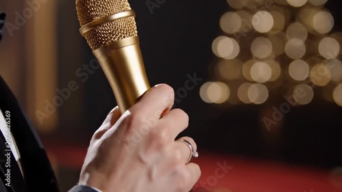 Hand holding golden microphone on stage at evening event