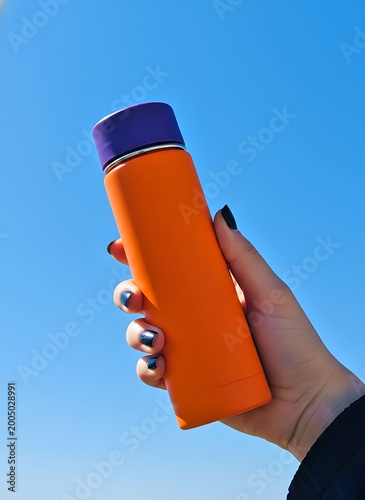 Vibrant Orange Reusable Water Bottle Mockup Held in Hand Against Clear Blue Sky for Summer Hydration
