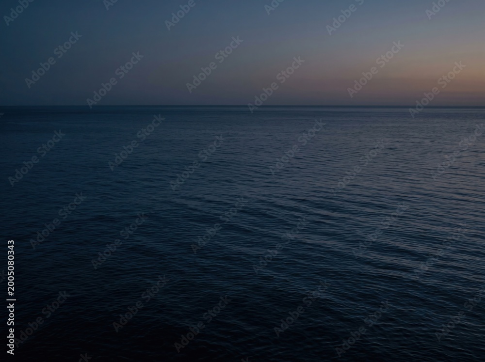Fototapeta premium Tranquil expanse of the open ocean at dusk, where the deep blue water meets the fading horizon under a vast, silent sky, conveying solitude and natural beauty