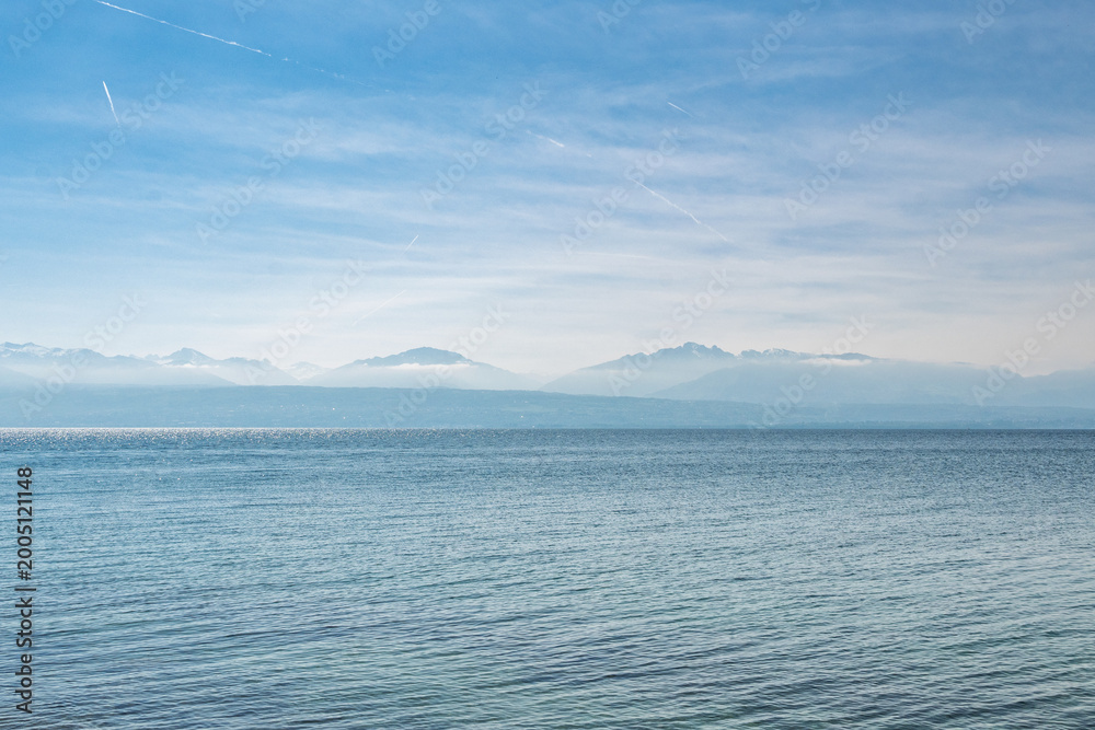 Obraz premium Vue panoramique sur le lac Léman et les Alpes françaises depuis Saint-Prex sous un ciel voilé, Suisse