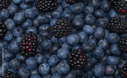 A dark background of fresh blueberries, blueberries and blackberries close up, fills the frame.