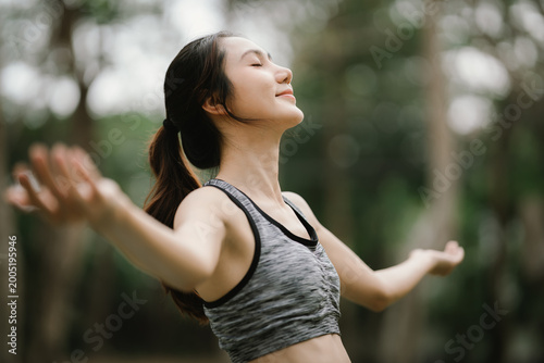 Quadro su tela Young Asian woman enjoying fresh air in a green park, eyes closed and arms open, expressing relaxation, mindfulness, and a healthy outdoor lifestyle
