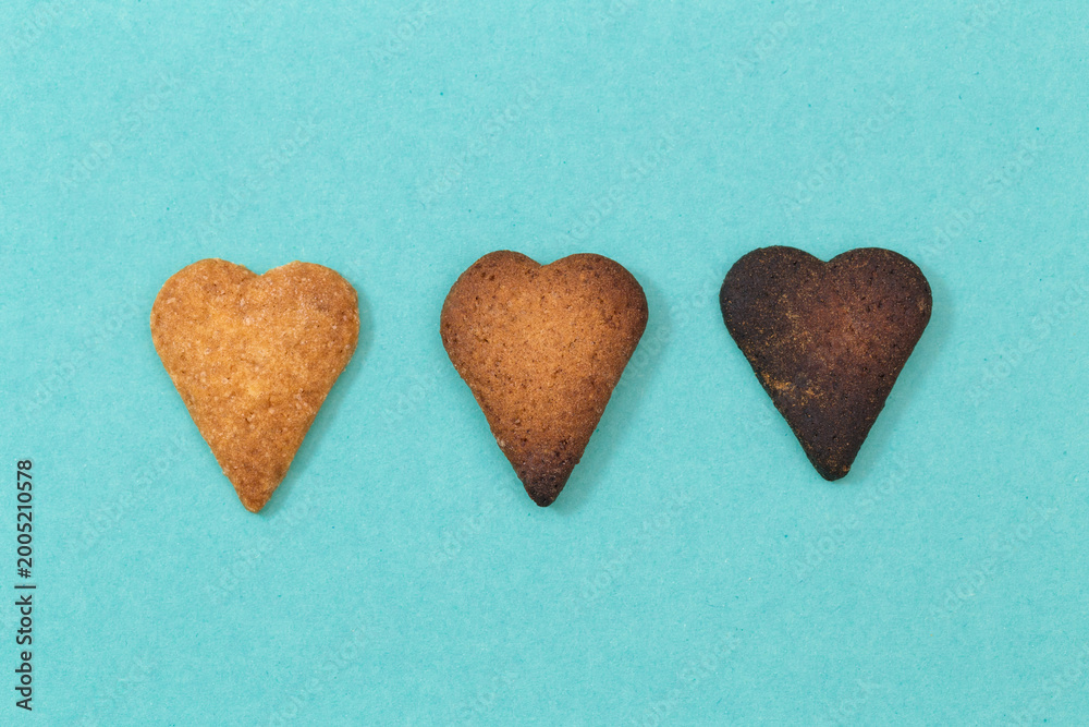 Obraz premium Three heart-shaped cookies in different baking stages on a blue background