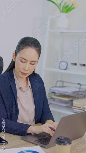 A professional middle-aged businesswoman is using a laptop sitting at her desk.