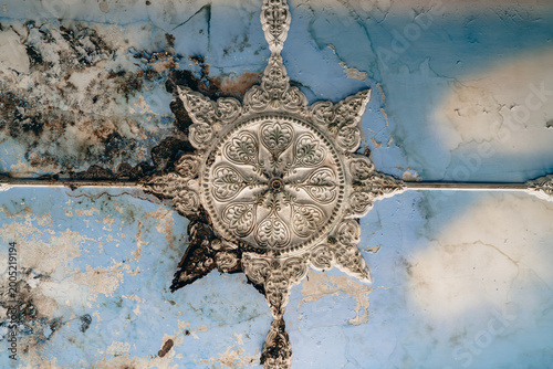 Damaged ornate ceiling medallion on cracked blue plaster, mold decay, vintage architectural detail, restoration texture background. 
