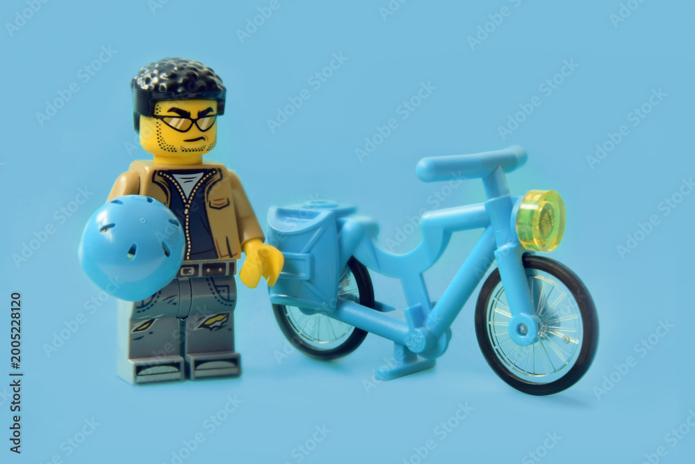 Naklejka premium Lego minifigure of biker with hardhat and bicycle or bike isolated on blue. Editorial illustrative image of popular plastic toy constructor for children.
