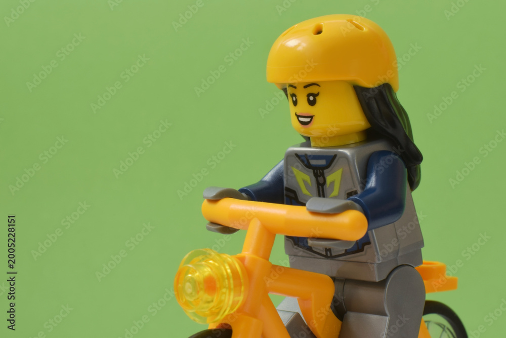 Fototapeta premium Lego minifigure of biker in yellow hardhat and bicycle or bike isolated on green. Editorial illustrative image of popular plastic toy constructor for children.