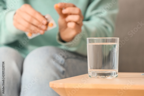 Foto Glass of water on table against young woman with pills, closeup