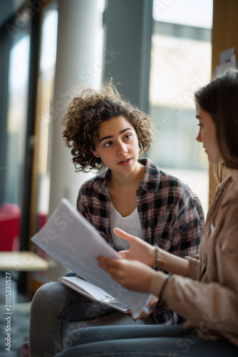 Professional scene of gen z female student explaining homework to friend in university campus lounge, medium close-up educational collaboration moment, natural window lighting, modern campus interior