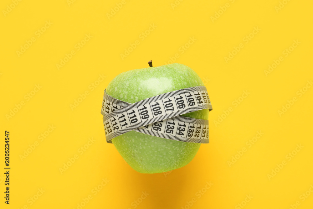 Fototapeta premium Fresh apple with white measuring tape on yellow background. Diet concept