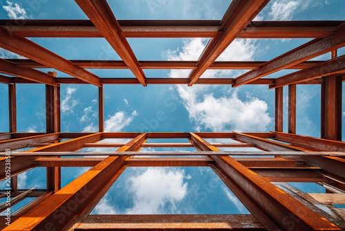 Looking up through rusty steel beams at fluffy white clouds in a blue sky