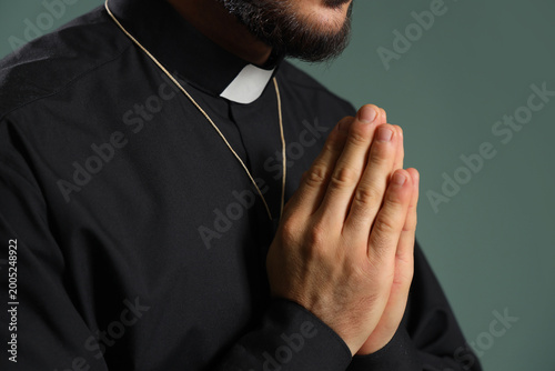 Obraz na płótnie Young priest praying on green background, closeup