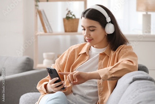 Pretty young woman with mobile phone and headphones listening to audiobook on...