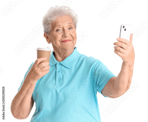 Senior woman with cup of coffee and mobile phone on white background