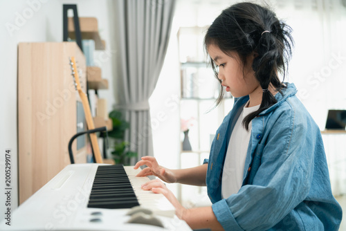 Young girl plays piano at home in cozy living room while wearing a denim jacket and focusing on her musical practice and creativity development
