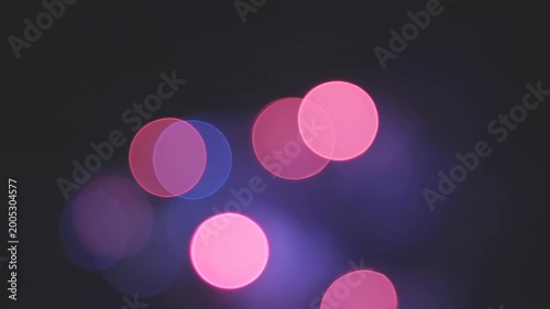 Soft luminous circles of pink and blue light gently shimmer and drift through the dark, creating an abstract bokeh glow at night