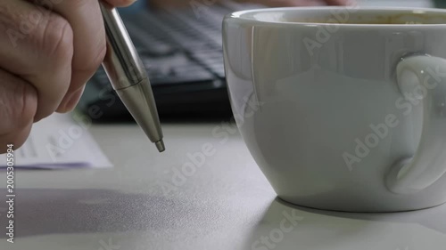 A hand meticulously taps a polished silver pen against a clean sheet of paper