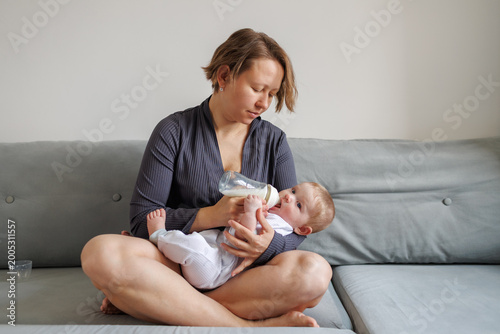 Full shot of a woman sitting cross-legged on a sofa feeding her baby