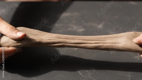 Hands kneading and stretching pottery clay on workshop table