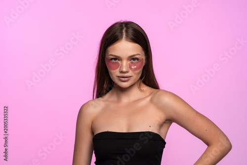 Young woman applying pink eye patches for skincare routine, focusing on beauty, wellness, and self-care