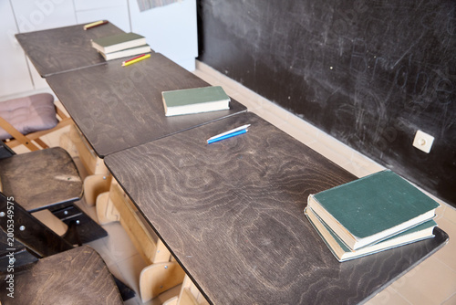 Obraz na płótnie Empty classroom desks with books and pens against blackboard wall