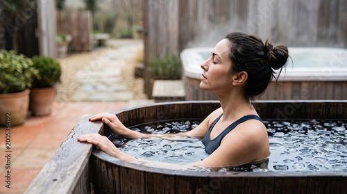 Woman taking a cold plunge at a recovery room concept. A woman relaxes in a wooden hot tub surrounded by nature.