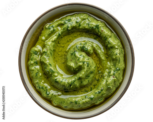 Close-up of bright green pesto in a white bowl with spoon fresh herbs