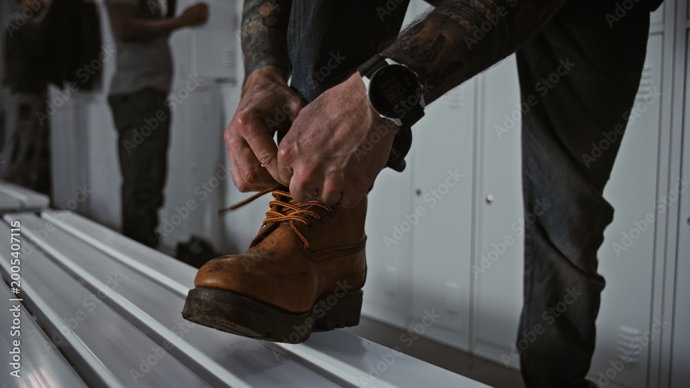 Fototapeta premium Close Up of Industrial Safety Boots. Worker In Professional Locker Room Ties Laces of Heavy Duty Brown Leather Safety Boots, Focusing on Footwear Reliability, Workplace Safety. Industrial Preparation.