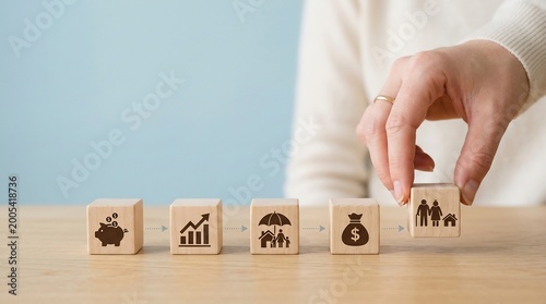 Wooden blocks featuring financial icons are arranged in a sequence as a hand completes the final step of a strategic plan, symbolizing the path toward achieving financial stability and long-term.