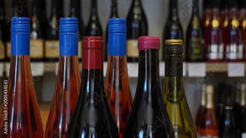 Rows of wine bottles with colorful caps in a wine cellar. Assorted wine bottle necks focusing on colorful seals on shelves.