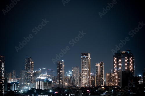 Modern highrise multi storey skyscrapers at night with lights shining through showcasing growth of apartments, buildings, houses and shopping centers in cities like gurgaon, delhi, bangalore, hyderaba