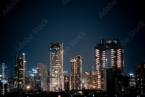 Fotografie Modern highrise multi storey skyscrapers at night with lights shining through sh