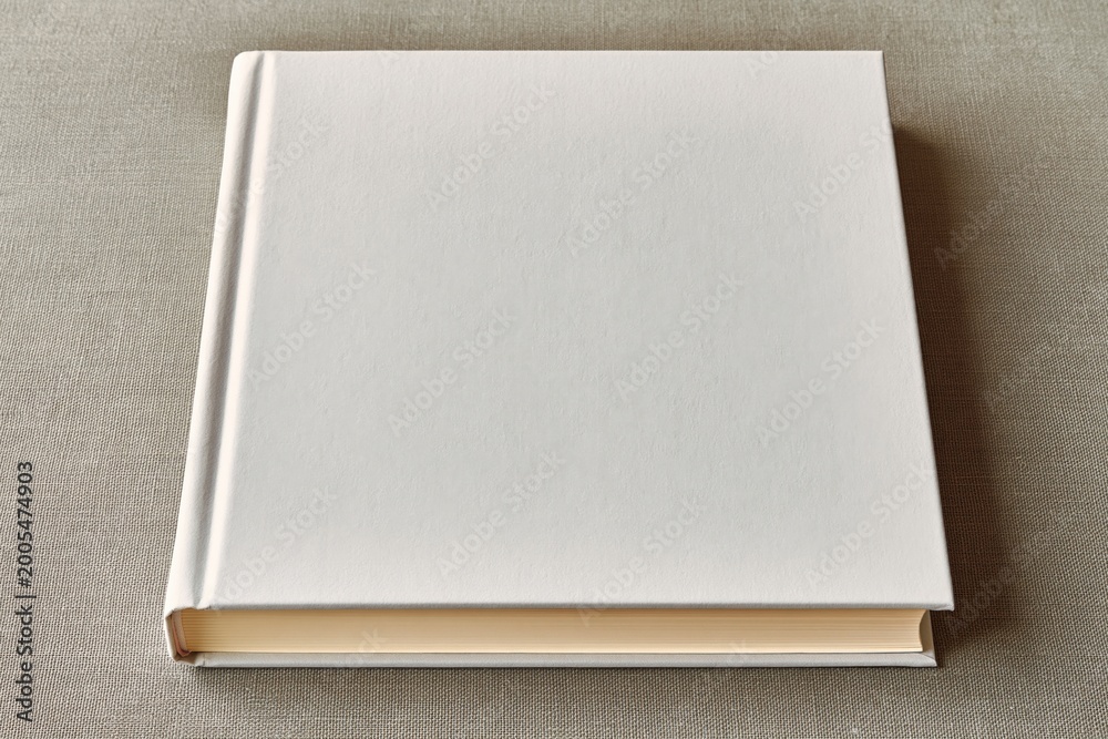 Fototapeta premium Blank white hardcover book lying flat on a textured surface, ready for custom design and branding