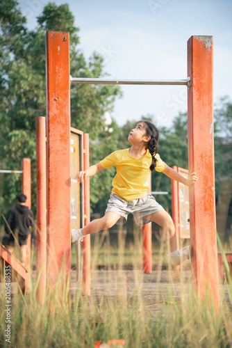 Young Girl Playing on Outdoor Gym Equipment in a Park, Engaging in Physical Activity and Enjoying Nature in Bright Yellow Shirt