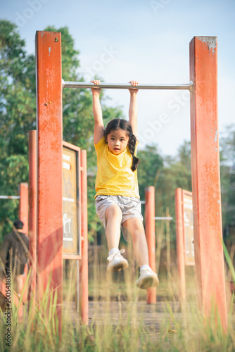Child Enjoys Outdoor Play on Monkey Bars in Bright Yellow T-Shirt Under Clear Sky Surrounded by Greenery at Community Park