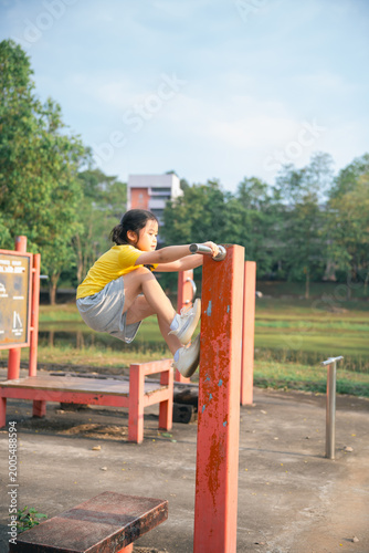 Energetic young child engaging in playful outdoor exercise on park fitness equipment, showcasing determination and physical activity in tranquil environment