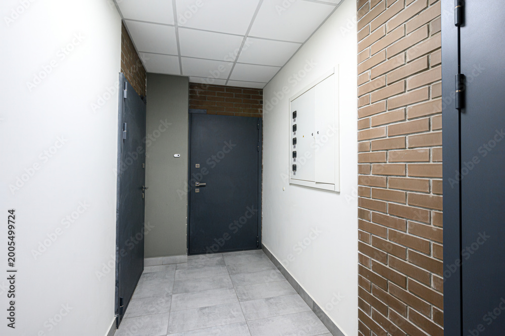 Fototapeta premium modern hallway with grey metal doors, brick accent wall, white paneled ceiling, light grey tiled floor, intercom panel, minimalist design, clean lines, neutral tones