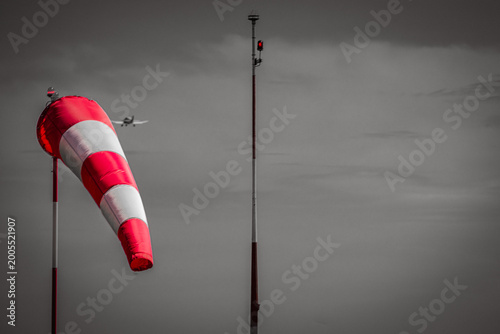 Tablou pe pânză Red and white windsock at an airfield with a small airplane in the background