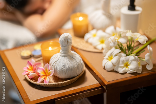 Herbal compress with candles and tropical flowers on wooden tray in spa setting.