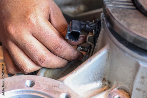 ​A close-up shot of a mechanic's hand carefully installing a plastic speed sensor onto a metal transmission casing using a bolt during a vehicle repair.