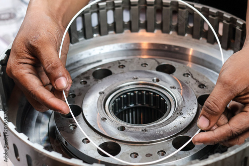 Close up shot of a technician's hands carefully fitting a large white rubber seal ring into the housing of an industrial metallic transmission gearbox during assembly.
