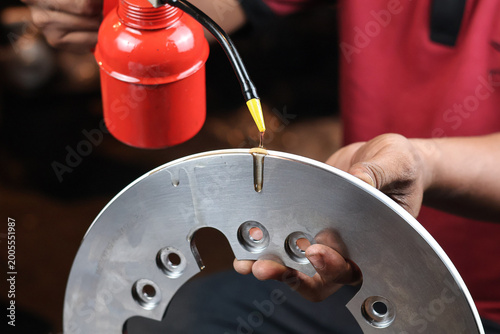 Fotografie Close up shot of a mechanic's hand pouring oil from a red oiler onto a metallic piston seal component to ensure proper lubrication during industrial engine maintenance