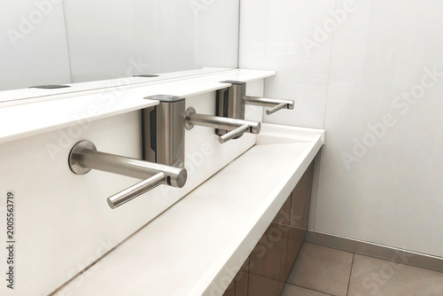 Minimalist public restroom with sleek stainless steel faucets and a white counter, emphasizing cleanliness, hygiene, and modern interior design.