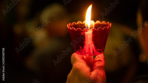 Obraz na płótnie A hand holding a burning candle in a red plastic cup during a night religious vigil or ceremony, creating a warm, spiritual glow
