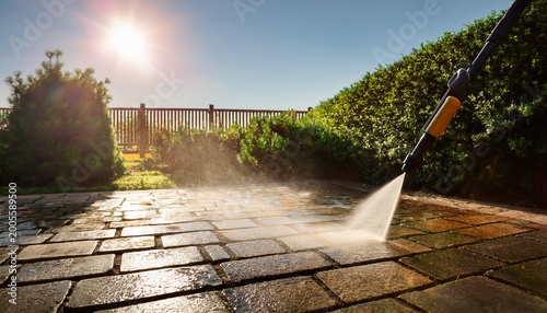 cleaning stone patio with a high pressure washer in a sunlit garden during spring maintenance