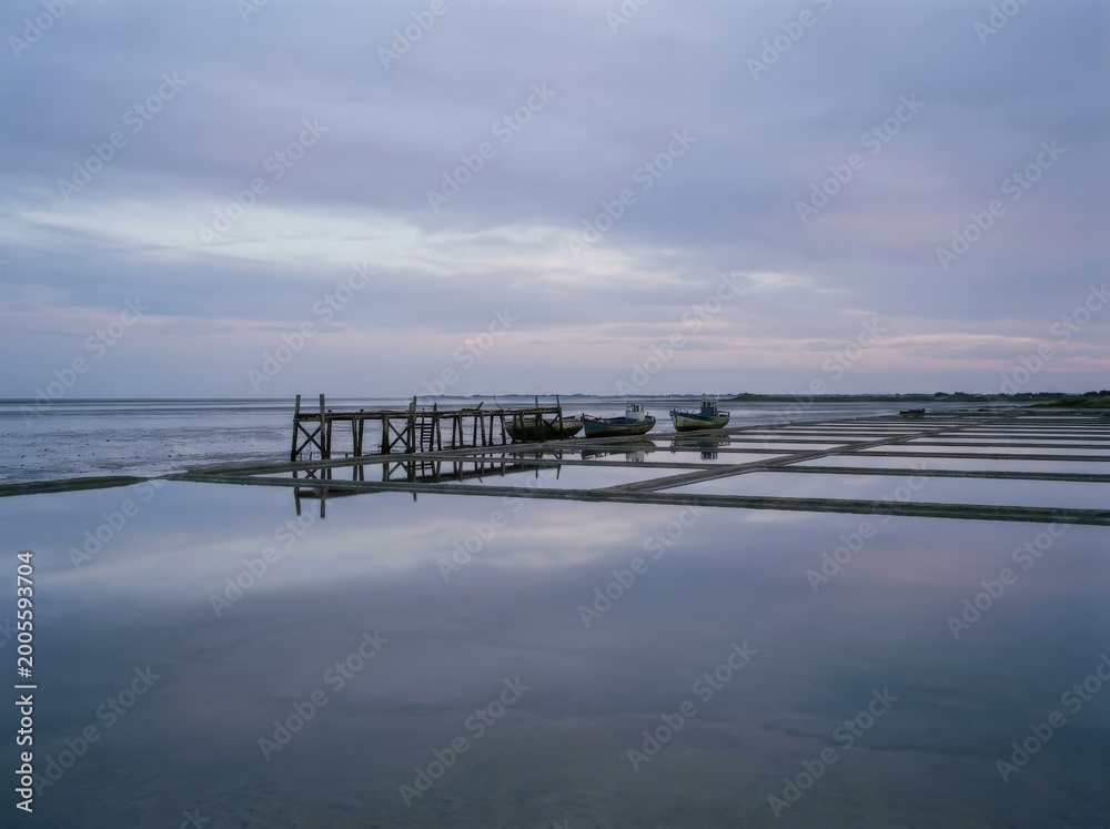 Fototapeta premium A serene coastal scene unfolds beneath a pastel sky, where wooden structure and boats find harmony with reflecting water.