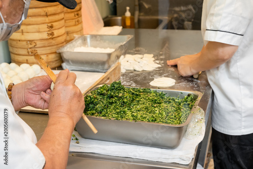Foto In a semi-open kitchen, chefs carefully prepare xiaolongbao by flattening dough into thin wrappers and filling them with minced pork and chives