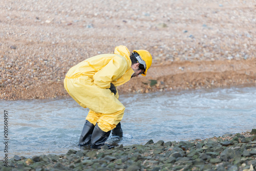 Workers in yellow suits and hard hats kneel by a river to collect water samples for testing at industrial site