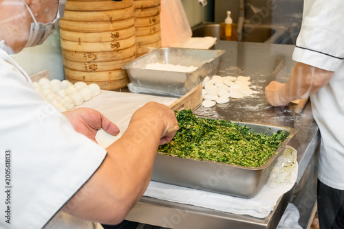 Fotografía In a semi-open kitchen, chefs carefully prepare xiaolongbao by flattening dough into thin wrappers and filling them with minced pork and chives