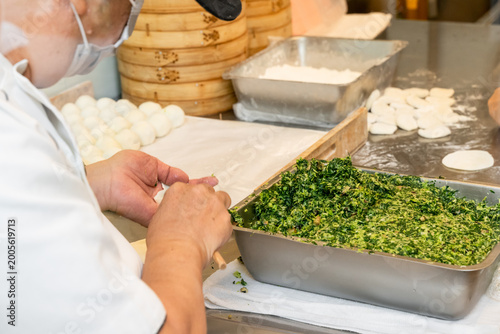 Bilde på lerret In a semi-open kitchen, chefs carefully prepare xiaolongbao by flattening dough into thin wrappers and filling them with minced pork and chives